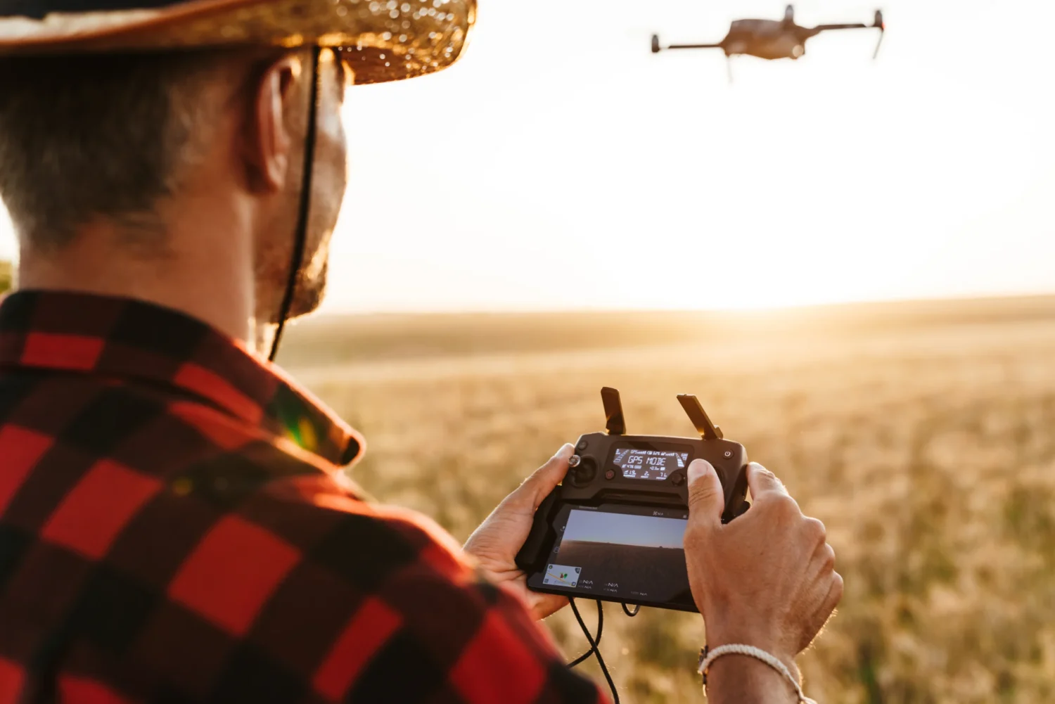 Image from back of focused man in straw hat using drone while standing at cereal field Image from back of focused man in straw hat using drone while standing at cereal field