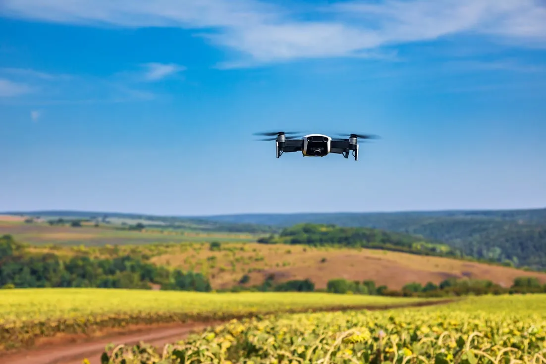 A drone flying above vibrant green fields under a clear blue sky, surveying the agricultural landscape below.