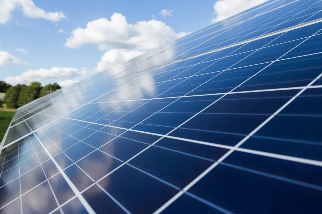 Close-up of blue solar panels reflecting clouds under a bright sky, highlighting renewable energy technology in an outdoor setting.